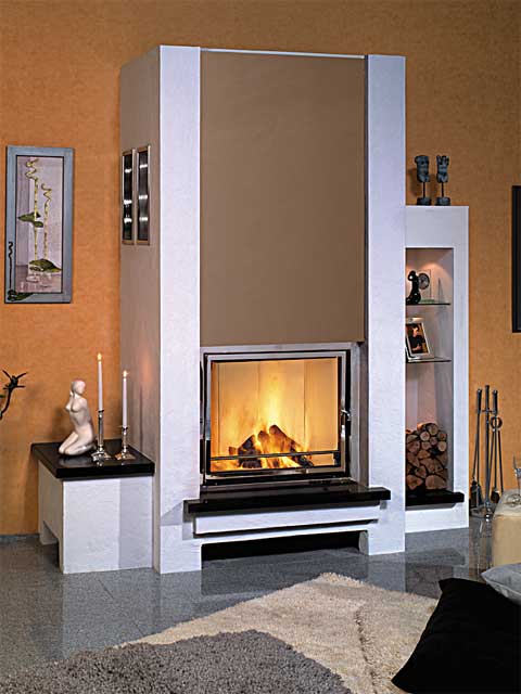 Nowoczesny, biały kominek z brązowym panelem i paleniskiem za szybą, uzupełniony o elementy dekoracyjne jak figurka i świece na bocznej półce oraz drewno i akcesoria kominkowe w niszy obok.